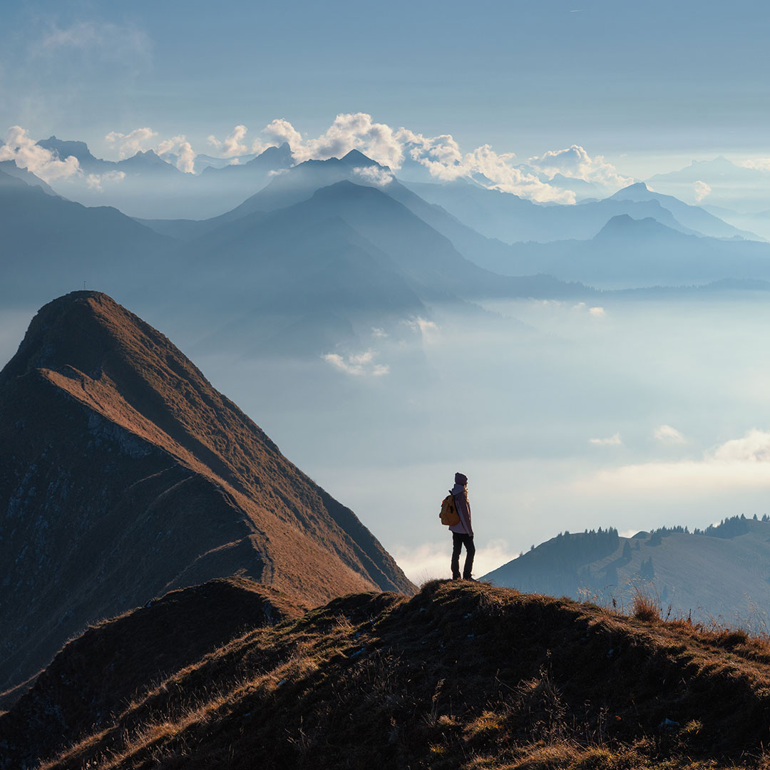 Ein Landschaftsbild, bei dem eine Person auf einem Berg steht und in die Ferne schaut